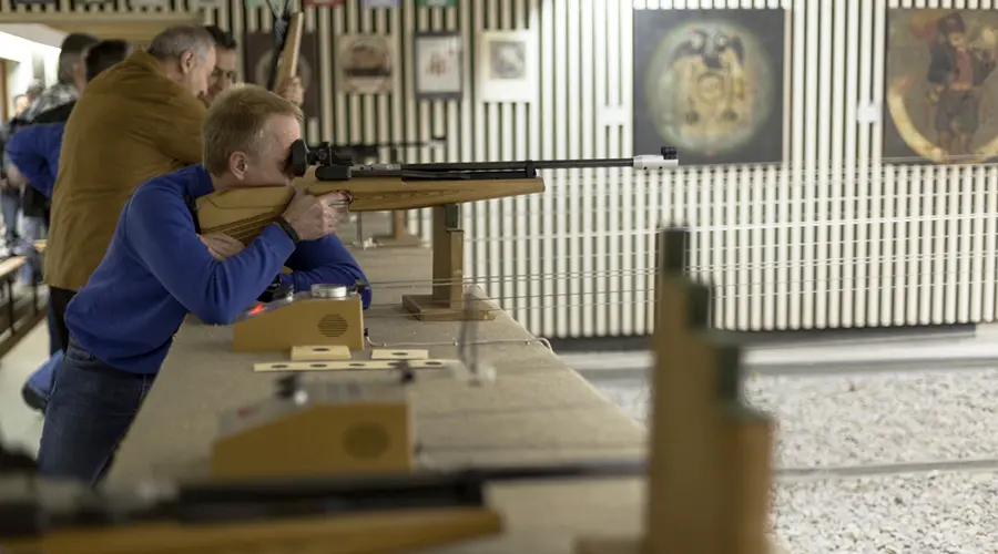 Ein Gast am Luftgewehr im Schießstand, betreut von einem Mitglied der Gilde